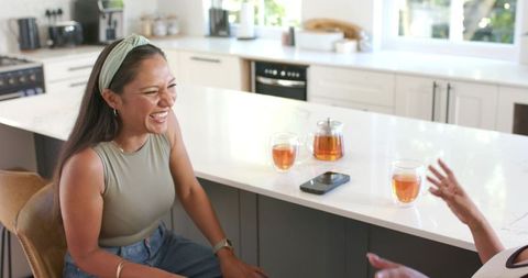 Laughing woman chatting at bright kitchen island with tea, phone and modern decor