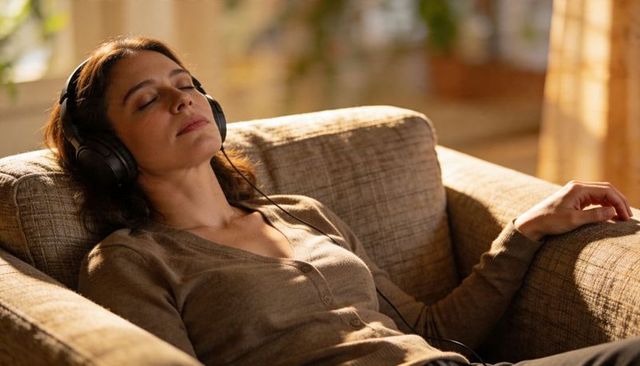 Female lounging on couch wearing headphones enjoying music in sun-drenched living room
