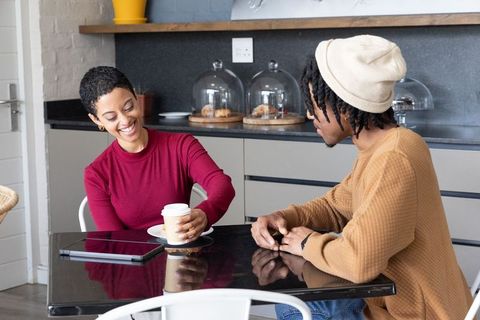 Smiling friends sharing coffee at modern cafe table with tablet and pastries
