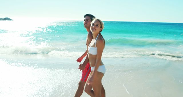 Couple wearing swimsuits walking together along beach enjoying sunny weather. Ideal for travel ads, vacation promotions, adventure blogs, or content related to relaxation and outdoor activities.