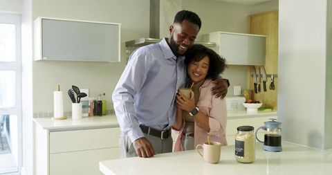 Couple sharing morning coffee and embracing at bright kitchen island, smiling