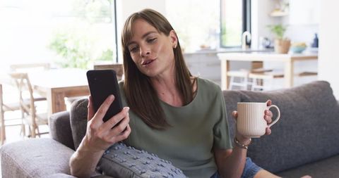 Middle-Aged Woman Relaxing with Smartphone and Coffee at Home