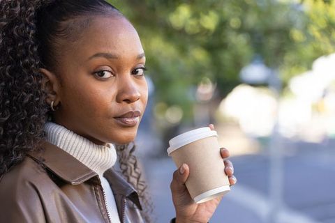 African american woman holding coffee cup on urban sidewalk wearing leather jacket