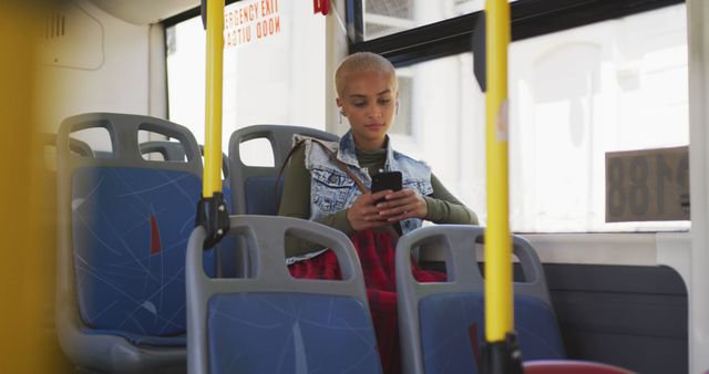 Biracial woman sitting in bus and using smartphone. Street style, modern urban lifestyle, communication and transport.