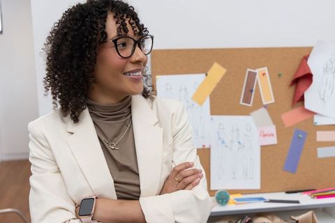 African american fashion designer standing confidently in studio with corkboard sketches