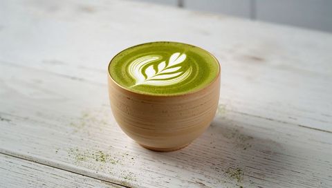 Ceramic cup of matcha latte with leaf latte art on rustic white wood table, minimalist