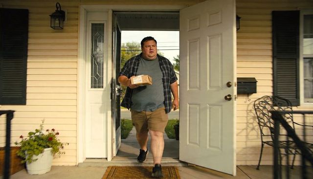 Man walking onto porch holding parcel at suburban home on sunny day