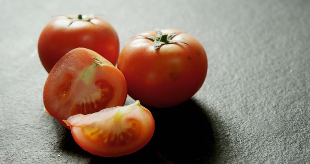 Fresh tomatoes are displayed on a dark surface, one sliced to reveal the ripe interior - Download Free Stock Photos Pikwizard.com