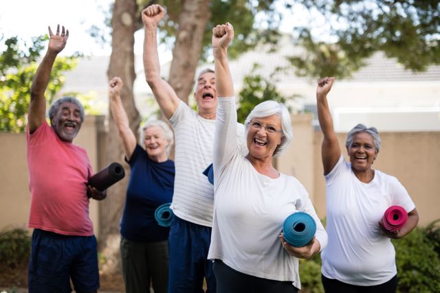 Group of multi-ethnic seniors raising arms and carrying exercise mats in a park. Ideal for promoting senior fitness programs, healthy lifestyles, community activities, and wellness events.