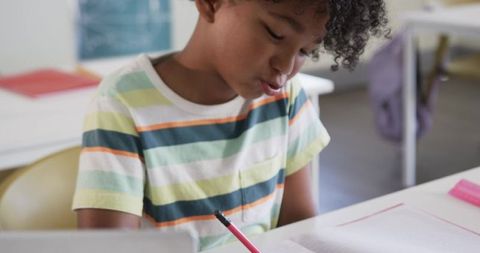 African American Boy Writing in Workbook at Classroom Desk Concentrating on Schoolwork
