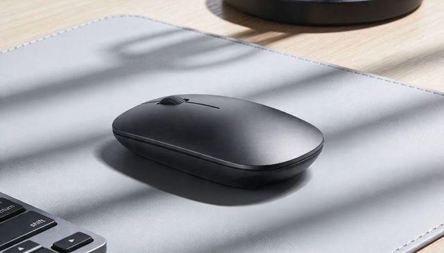 Matte black wireless mouse on gray desk mat with soft sunlight and minimal design