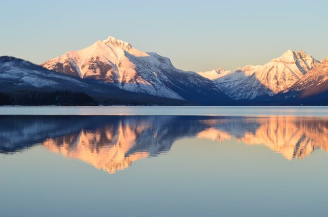 Peaceful snowy mountain peaks perfectly mirrored in tranquil lake during early morning light. Ideal for nature-themed projects, travel advertisements, or background images promoting serenity and beauty in natural environments.