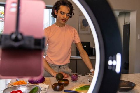 Influencer filming culinary tutorial at home kitchen island with ring light and smartphone