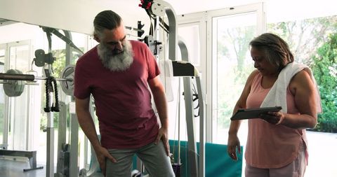 Senior couple exercising in gym with tablet guidance