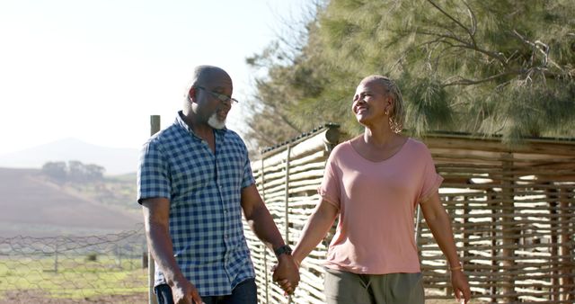 Happy senior african american couple holding hands walking and talking in sunny garden. Retirement,wellbeing, summer and active senior lifestyle, unaltered,copy space.