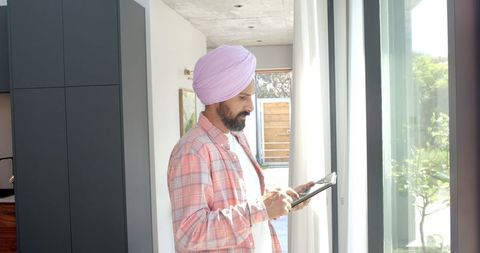 Man in turban using tablet by window in modern home