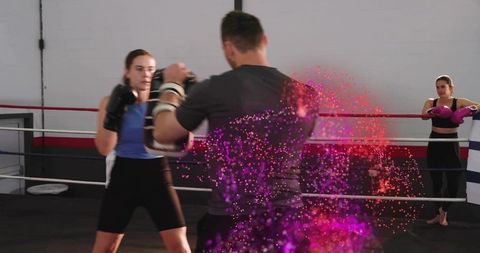Female boxer training with coach holding pads in boxing ring with pink purple effect