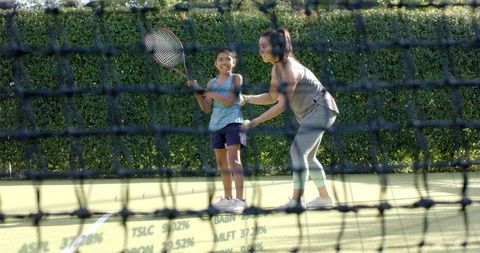 Female Tennis Coach Teaching Young Girl Racket Skills on Outdoor Court Through Net
