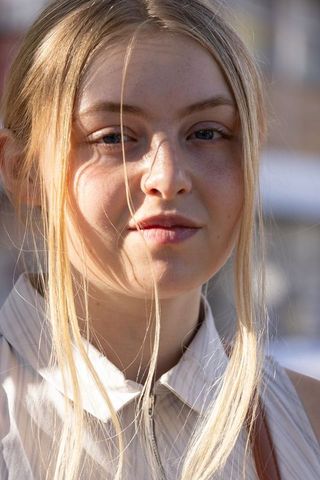 Sunlit blonde woman posing in urban portrait, freckles, loose hair strands, collared top