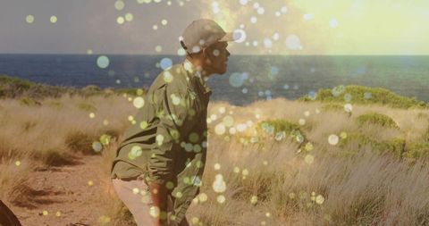 Leaning man gazing toward ocean on coastal path with warm bokeh light