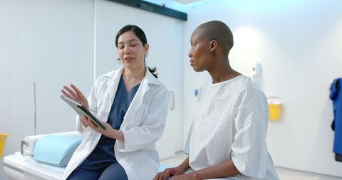 Diverse female clinician consulting with patient on tablet in modern medical exam room