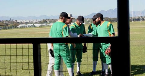 Baseball team huddling with coach on grass field planning game strategy and team unity