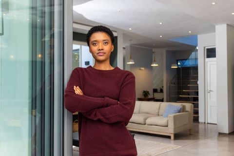 Confident african american woman standing by glass door in modern open-plan living room