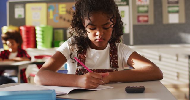 Portrait of biracial schoolgirl sitting in class, making notes, looking at camera. children at primary school in summer.
