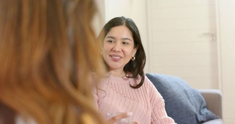 Women sharing warm conversation on cozy living room sofa smiling and holding glass
