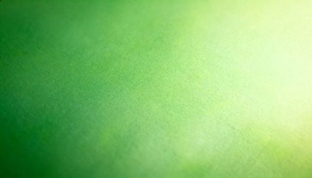 Textured green paper close-up showing diagonal gradient and soft grain for background use