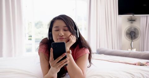 Woman Relaxing in Bedroom Holding Smartphone with Headphones