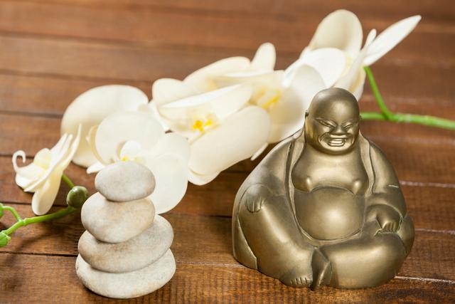 Laughing buddha figurine with pebbles stone and flower on wooden table