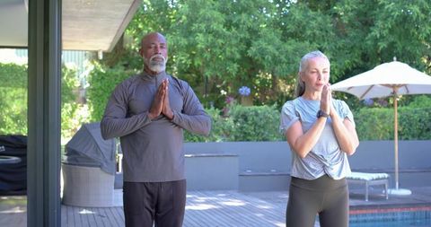 Mature couple practicing yoga on poolside deck meditating for mindfulness and wellness