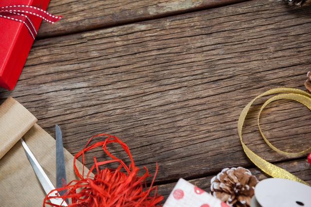 Christmas decorations, including ribbons, pine cones, and gift wrapping materials, are spread out on a wooden table. This image can be used for holiday-related promotions, gift-wrapping tutorials, or festive greeting cards.