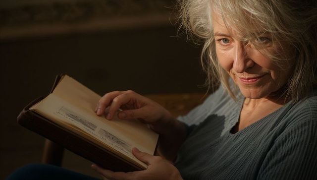 Senior woman holding family album, reflecting with gentle smile in warm living room light