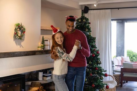 Festive Couple Dancing in Warm Holiday Sweaters by Christmas Fireplace