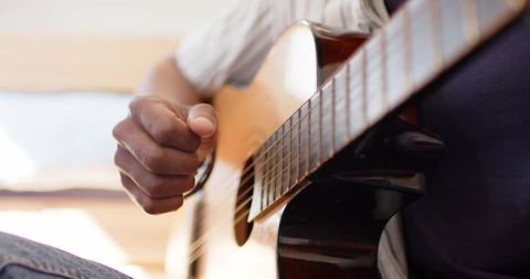 Close-up hand strumming acoustic guitar with warm wood grain and soft bokeh background