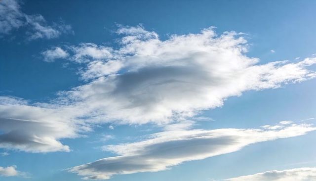 Sunlit Lenticular Clouds Floating Across Blue Sky with Wispy Cirrus Layers