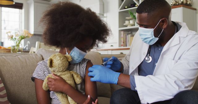 African american doctor wearing face mask injection covid-19 vaccine to girl at home. concept of corona virus vaccine and treatment during pandemic.