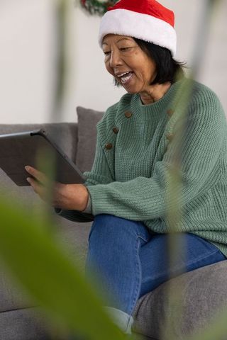Happy Asian Woman Wearing Santa Hat Using Tablet on Sofa