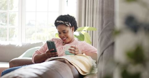 Relaxed Woman Smiling at Phone with Mug in Cozy Living Room