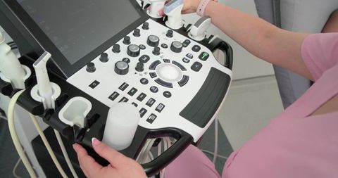 Clinician operating ultrasound console holding transducer wearing pink scrubs