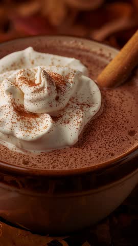 Vertical video capturing twisting cinnamon stick dusting cocoa over whipped-cream topped hot chocola