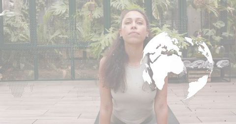 Woman practicing yoga backbend in glass conservatory with globe overlay for global wellness