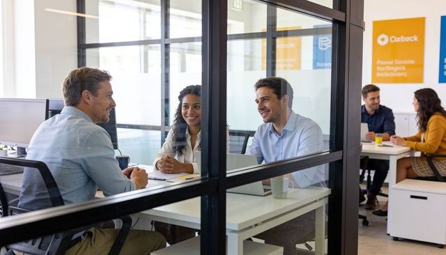 Business team collaborating through glass partition in modern open-plan office meeting