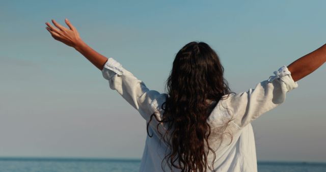 Woman with arms raised towards sky feeling freedom near the ocean - Download Free Stock Images Pikwizard.com