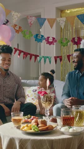 Family laughing and clapping while guest tapping knees at colorful home party vertical video