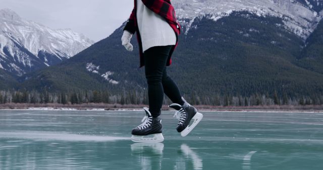 Person ice skating on a frozen lake, with copy space. Outdoor winter activity captured with a scenic mountain backdrop.