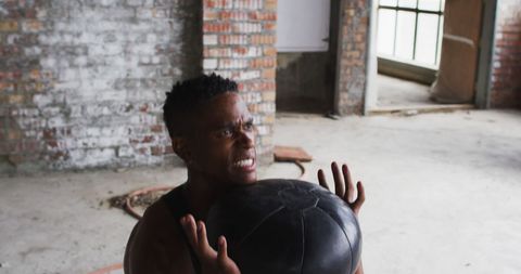 man performing intense exercise with a medicine ball in empty urban building, showcasing determination and a focus on fitness. ideal for promoting workout programs, urban fitness classes, or active lifestyle brands.