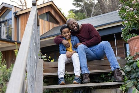 African american father and son sitting on steps laughing and bonding at modern home